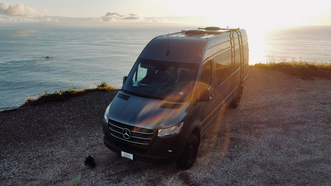 Experience van life! An rv rental Mercedes Sprinter camper van overlooks the ocean at sunset from a cliff.