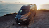 Experience van life! An rv rental Mercedes Sprinter camper van overlooks the ocean at sunset from a cliff.