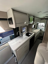 Modern RV rental interior: A bright, compact space with kitchenette, sink, cooktop, and bed, ideal for road trips.