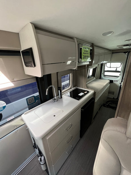 Modern RV rental interior: A bright, compact space with kitchenette, sink, cooktop, and bed, ideal for road trips.