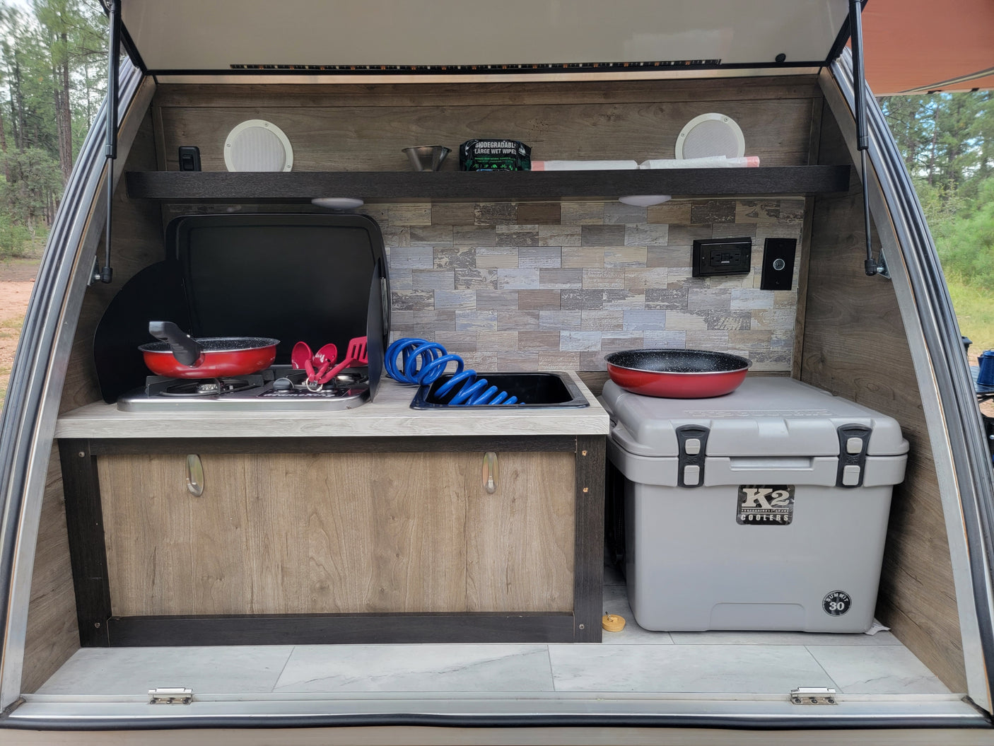 This RV rental's outdoor kitchen features a stove, sink, and cooler for camping adventures.