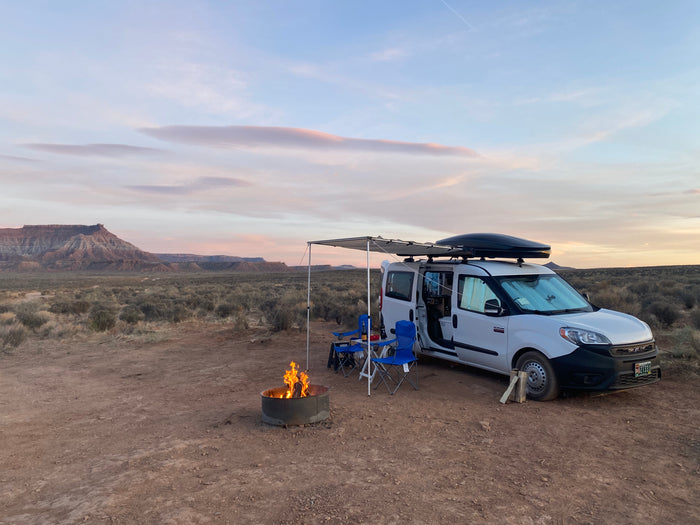 Ram ProMaster City RV rental van set up for desert camping with a warm campfire at sunset.