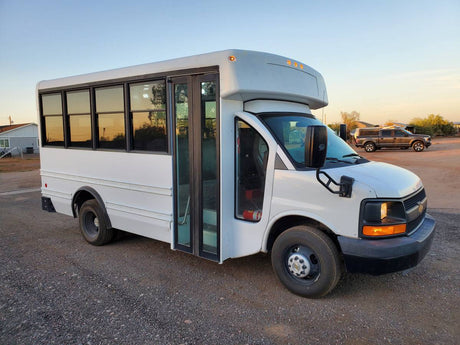 This white shuttle bus, ideal for RV rental or a custom camper van conversion, is parked on gravel.