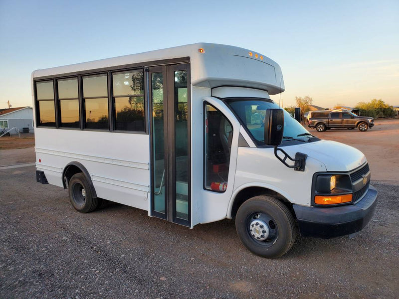 This white shuttle bus, ideal for RV rental or a custom camper van conversion, is parked on gravel. — photo 10