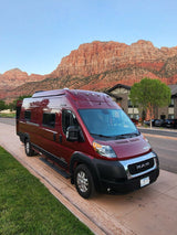 Red RV rental van parked with stunning Zion National Park mountains in the background. Perfect for travel adventures!