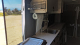 RV rental interior: Kitchenette with sink, paper towels, drying rack, and a bright screened window view.