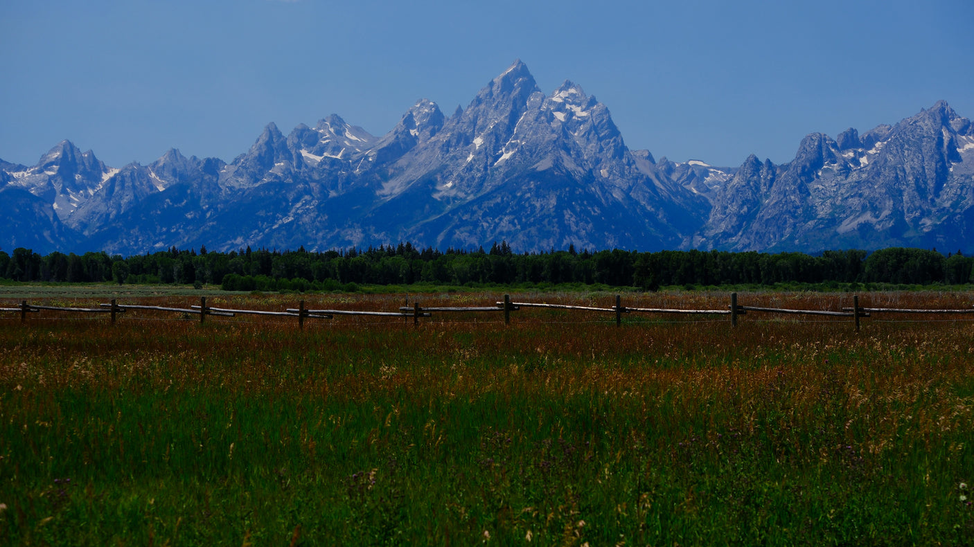 Explore the stunning Grand Teton mountains, green meadows, and wooden fence. Perfect scenery for your RV rental journey.