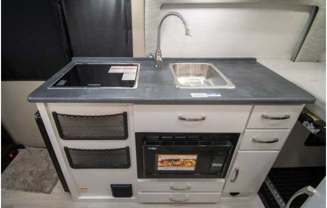 Discover the compact kitchen in this RV rental: electric stovetop, sink, microwave, and smart storage for your travels.