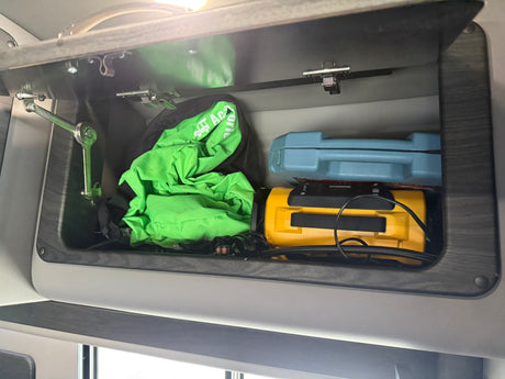 Overhead cabinet in an RV rental, holding a green emergency bag, blue case, and a yellow portable air compressor.