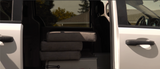 Inside an RV rental: three stacked gray cushions, likely a bed, visible through the open side door of the white van.
