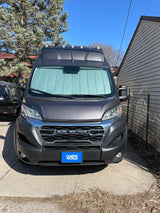 Front view of a dark gray Ram ProMaster camper van, likely an rv rental, parked in a sunny driveway with a sunshade.