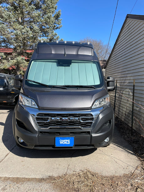 Front view of a dark gray Ram ProMaster camper van, likely an rv rental, parked in a sunny driveway with a sunshade.