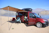 Experience freedom! Red camper van rv rental by a lake, setup with awning & chairs for ultimate outdoor comfort.