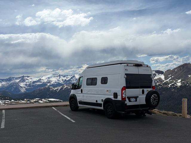 Experience mountain views with an rv rental. White camper van parked overlooking snow-capped peaks under clouds.|White Winnebago Solis Pocket rv rental with pop-top roof parked on a sunny cliffside overlooking the ocean and coast.|A white Winnebago Solis Pocket RV rental is parked on a vast