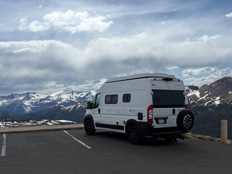Experience mountain views with an rv rental. White camper van parked overlooking snow-capped peaks under clouds.|White Winnebago Solis Pocket rv rental with pop-top roof parked on a sunny cliffside overlooking the ocean and coast.|A white Winnebago Solis Pocket RV rental is parked on a vast — photo 1