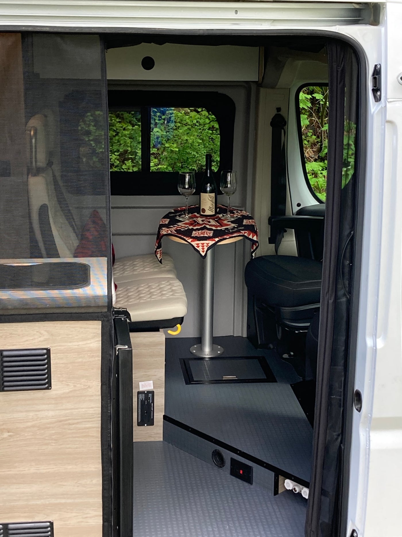  parked in a lush green forest. Interior visible.|Open side door of white Winnebago pop-top RV rental — photo 13