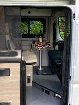 Step into this RV rental's cozy interior: dining table with wine, bed, and front swivel seat. Nature view outside.