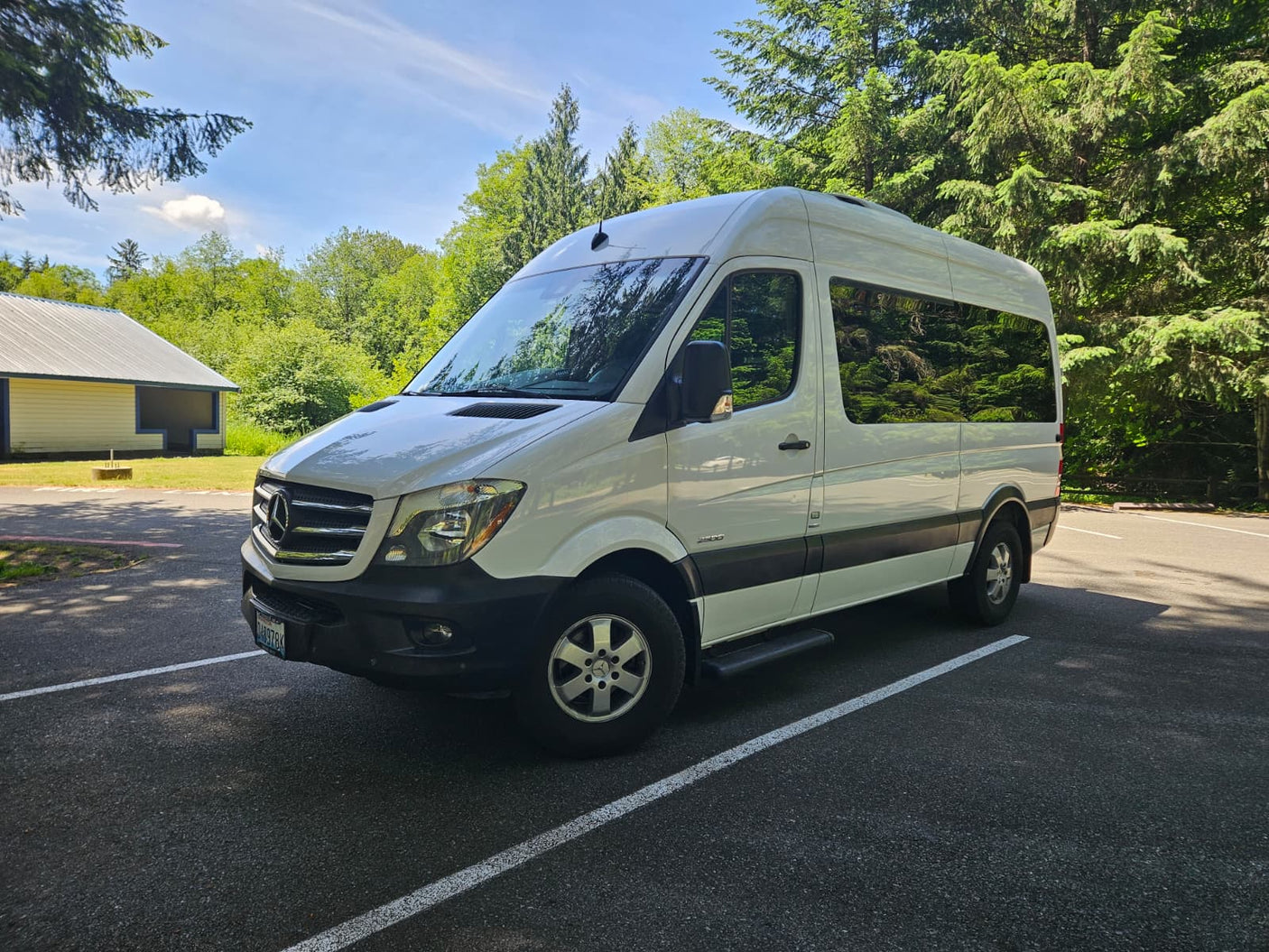 White Mercedes-Benz Sprinter RV rental, a camper van parked in a sunny outdoor setting with lush trees.