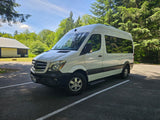 White Mercedes-Benz Sprinter RV rental, a camper van parked in a sunny outdoor setting with lush trees.