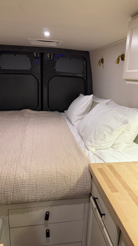 Cozy RV rental interior with a neatly made bed, stylish brass lights, and clever built-in storage solutions.