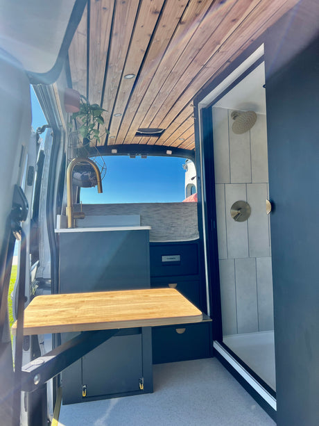 Modern rv rental interior: stylish kitchenette with golden faucet, wood ceiling, fold-out table, and full shower with elegant fixtures.