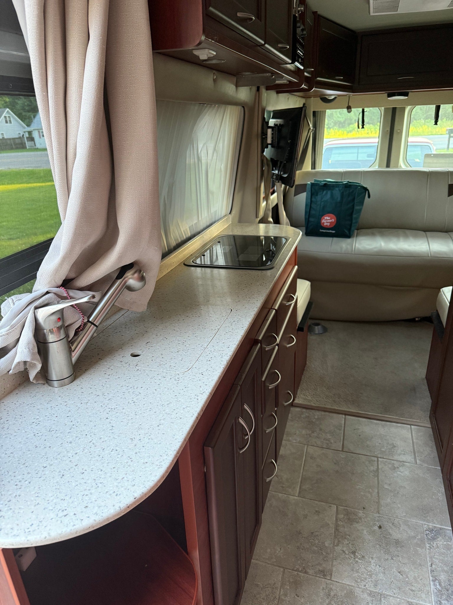Inside an RV rental, featuring a well-equipped kitchen with sink and stovetop, dark wood cabinets, and comfortable seating.