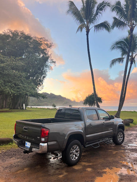 Gray Toyota Tacoma pickup on a muddy path at a tropical beach during sunset. An ideal setting for an RV rental adventure.