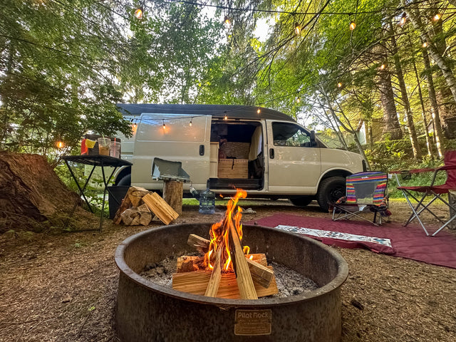 Cozy camping setup with a roaring campfire and string lights next to an RV rental van in the woods. Perfect outdoor adventure.|Cozy RV rental interior with wood details