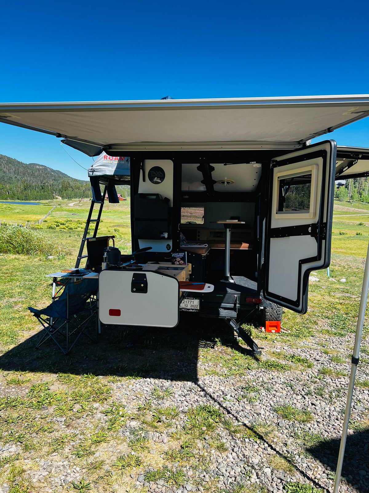This RV rental camper, with an open outdoor kitchen, rooftop tent, and awning, is perfectly set for a camping adventure amidst scenic nature. — photo 7