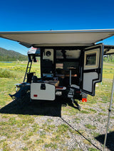 This RV rental camper, with an open outdoor kitchen, rooftop tent, and awning, is perfectly set for a camping adventure amidst scenic nature.