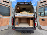 Spacious RV rental van with custom wood interior, cozy bed, and practical under-bed storage. Ready for adventures!