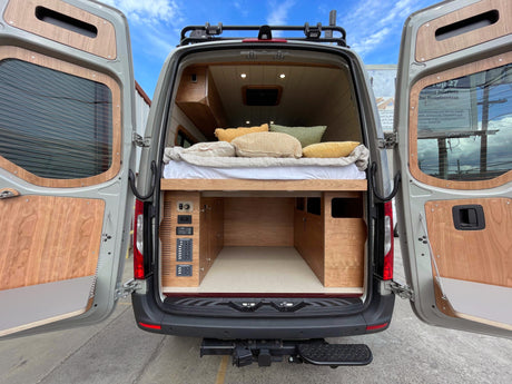 Spacious RV rental van with custom wood interior, cozy bed, and practical under-bed storage. Ready for adventures!