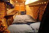 Step into this cozy RV rental's interior! Features a comfy bed, wood paneling, and a compact kitchen area with custom tiles.