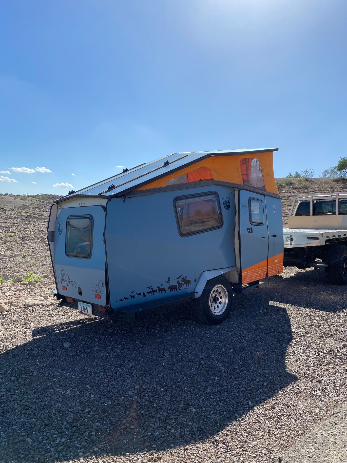 Unique gray & orange rv rental camper trailer with solar panels & pop-top, ready for outdoor adventure on rocky ground.