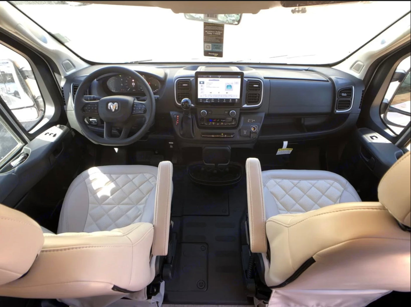Spacious RV rental cockpit: Features a modern dashboard, large screen, steering wheel, and quilted light-colored front seats.