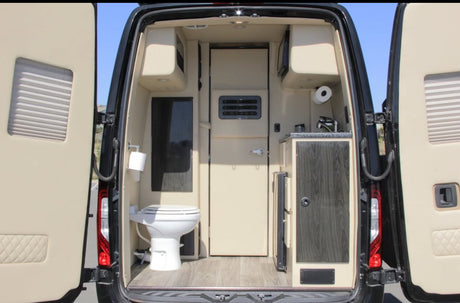 **RV rental**'s rear interior with open doors reveals a toilet, sink, and compact kitchen. Beige and dark wood design.