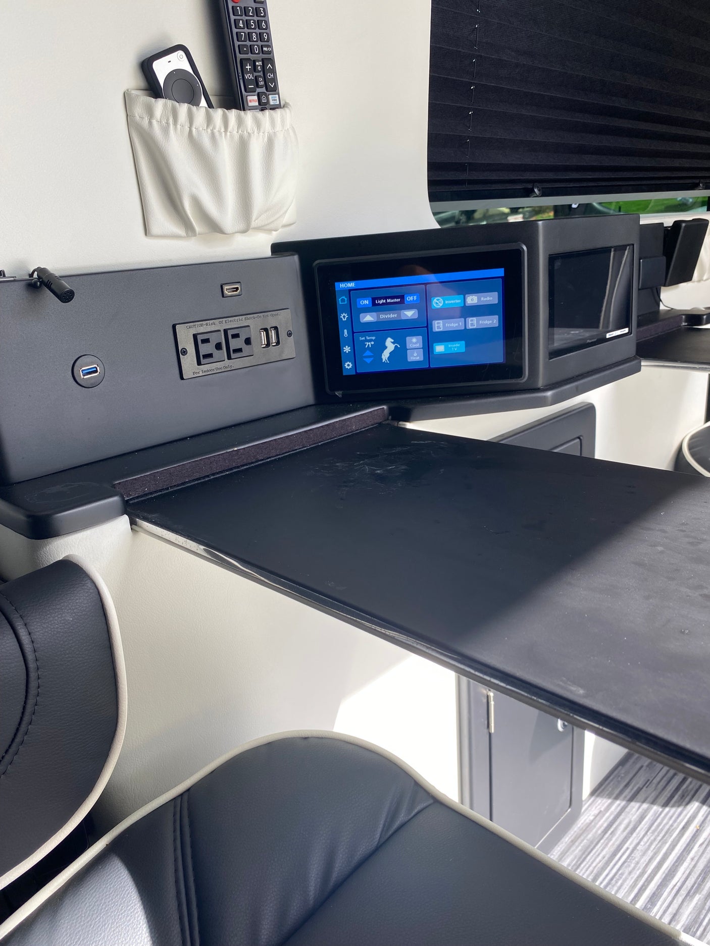 RV rental cabin with a modern control panel, power outlets, remotes, and seating, offering essential amenities for travel comfort.