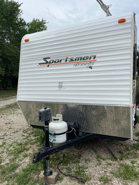 This white Sportsmen Classic travel trailer, seen from the front with its propane tank, is ideal for RV rental.