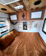 This cozy RV rental interior features a full bed with textured covers, patterned curtains, and custom wooden ceilings.