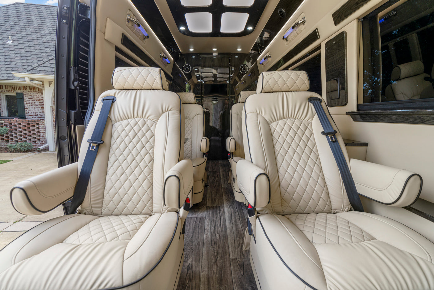 Spacious, luxury RV rental interior with cream quilted leather captain chairs, wood flooring, and ambient lighting.