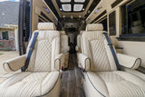 Spacious, luxury RV rental interior with cream quilted leather captain chairs, wood flooring, and ambient lighting.