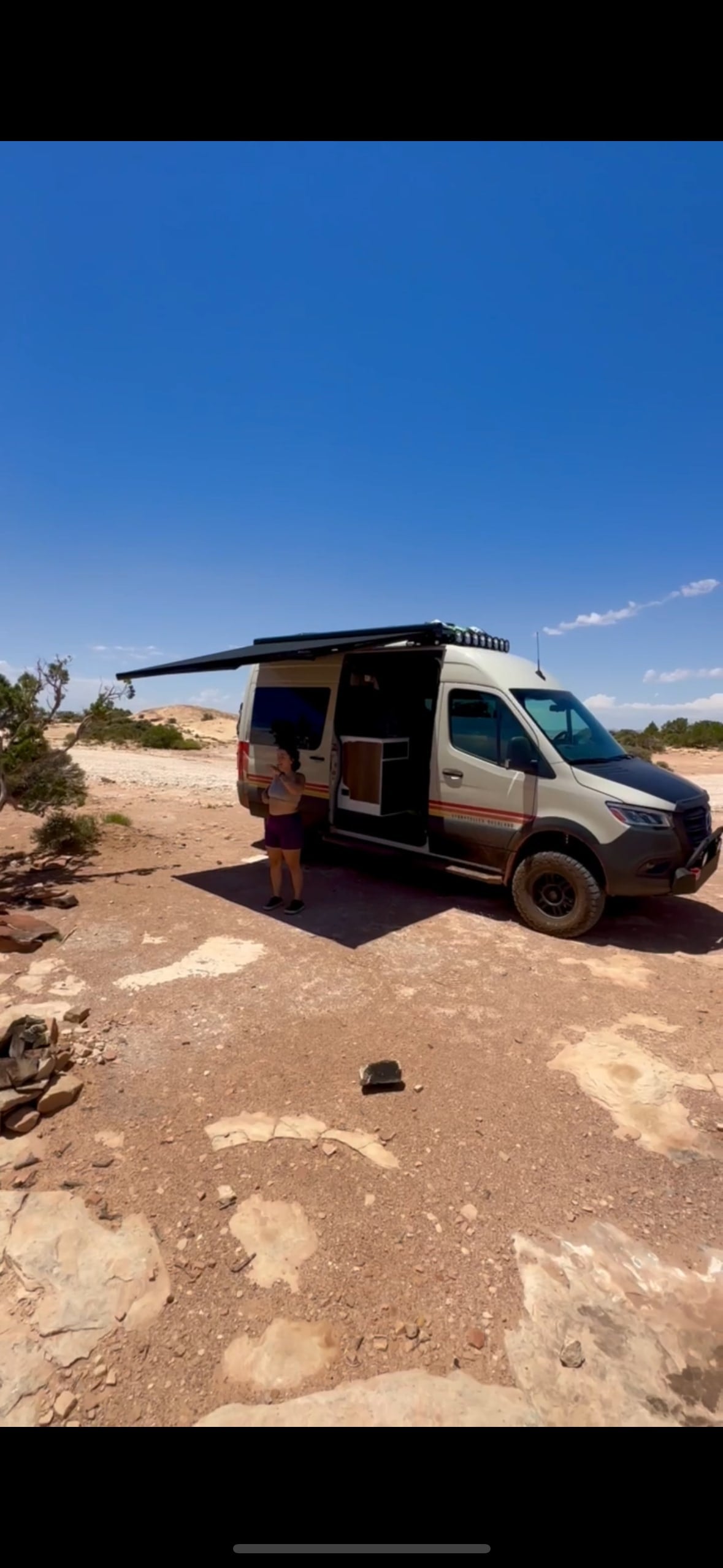 An RV rental van, awning extended, sits in a desert campsite. A person stands by its open door. Ready for van life adventures!