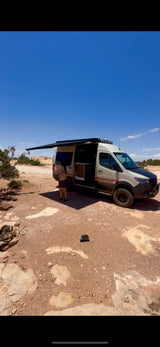An RV rental van, awning extended, sits in a desert campsite. A person stands by its open door. Ready for van life adventures!