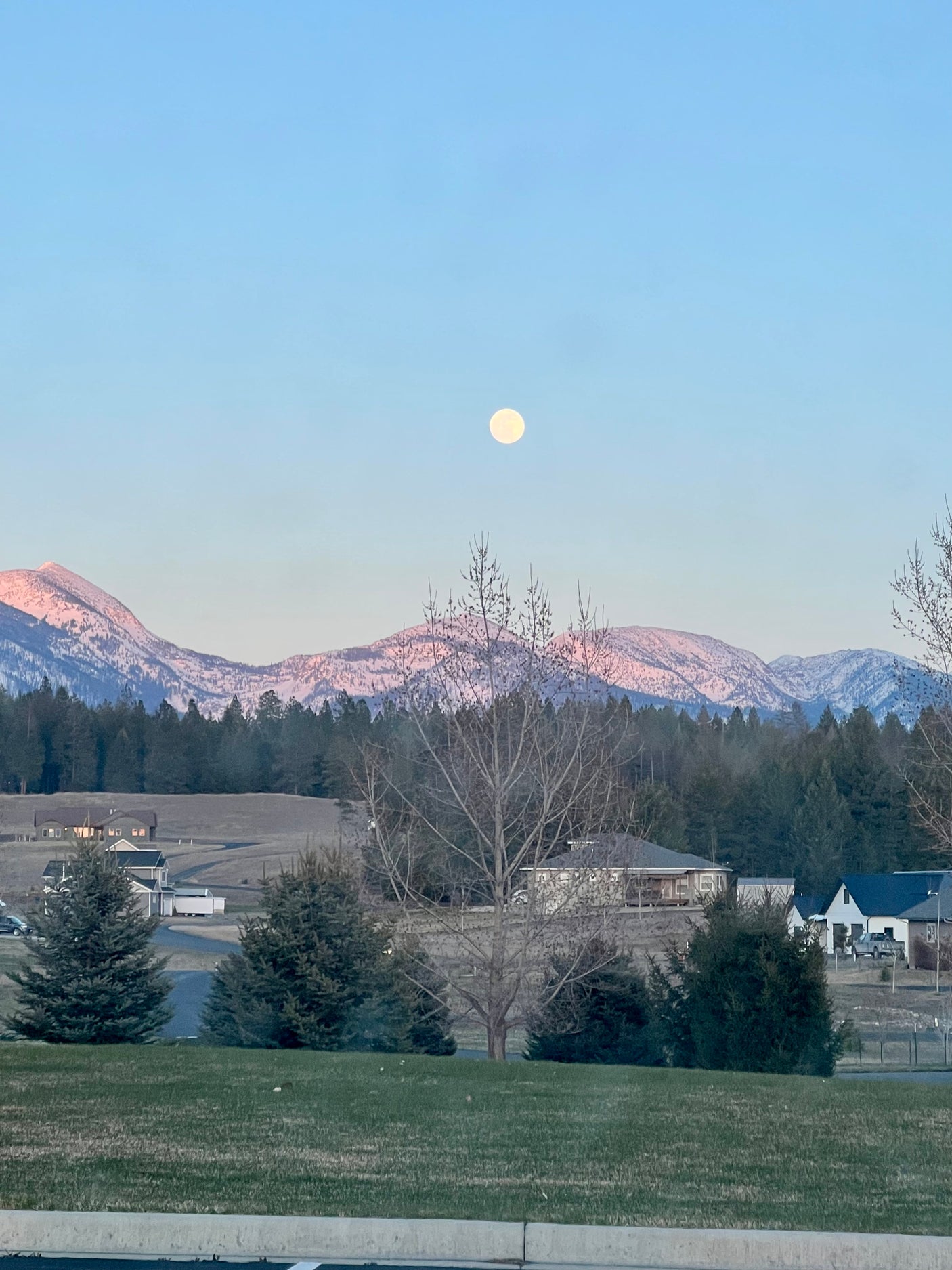A bright moon hangs above snow-capped mountains and homes at dusk. Experience peaceful views with an RV rental.