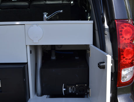 Inside an RV rental: a compact kitchen setup with sink, faucet, water tank, and accessible plumbing.