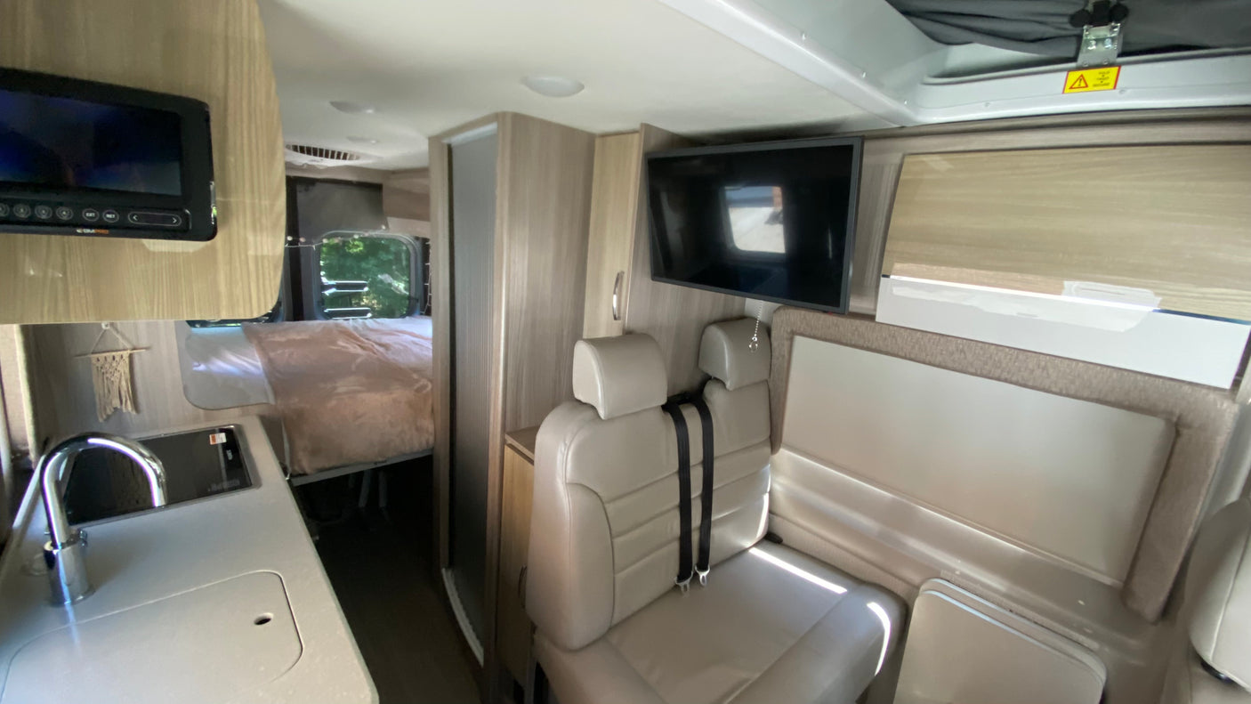 Explore this RV rental's versatile interior: a modern kitchenette, comfy seating with a TV, and a private rear bedroom awaits.
