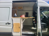 Spacious van conversion interior: custom kitchen with sink & fold-down table. Perfect RV rental for road trips.