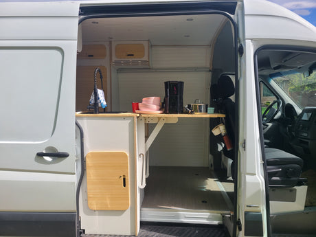 Spacious van conversion interior: custom kitchen with sink & fold-down table. Perfect RV rental for road trips.