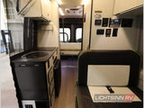 RV rental: view of a camper van's functional interior with kitchen, passenger seating, solar controls, and a rear bed.