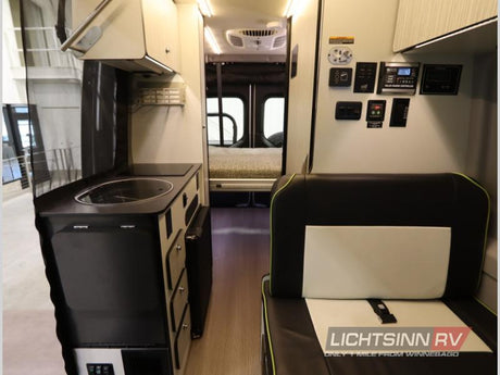 RV rental: view of a camper van's functional interior with kitchen, passenger seating, solar controls, and a rear bed.